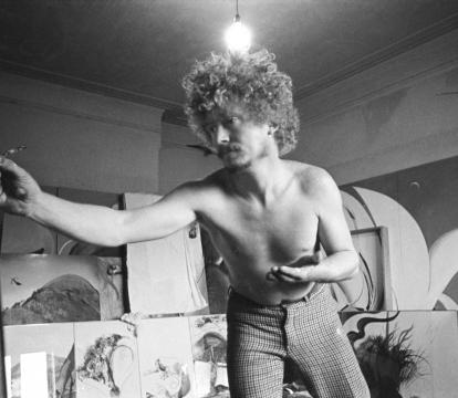 Brett Whiteley paints with a series of unfinished paintings in the background in black and white.
