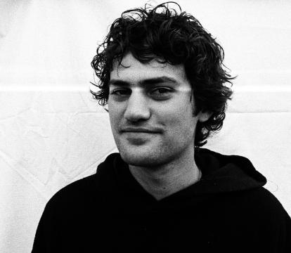 A close of up a white man with dark hair smiling, wearing a black hoodie.