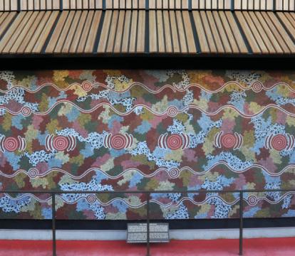 Possum Dreaming mural in pastel blues, red and greens, framed by red curtains, which are drawn to either side.