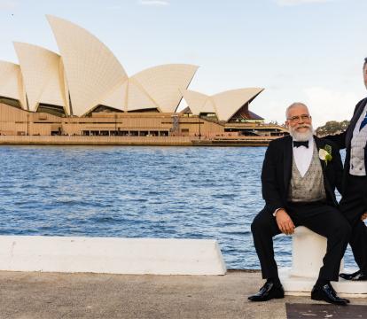 Two men stood in suits outside of the Sydney Opera House.