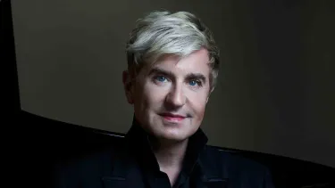 A person with short, blond hair and light skin is wearing a black jacket.