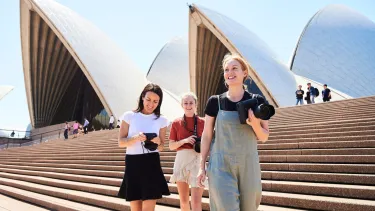 Three women with cameras walking down the steps of the Sydney Opera House.