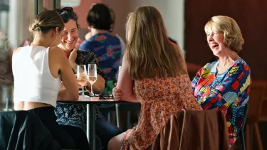 A group of women smile sitting at a table next to glasses of champagne.