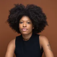 A headshot of Aliyah Knight wearing a black singlet against a bronze coloured background.