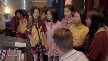 A man surrounded by school kids in a recording studio.