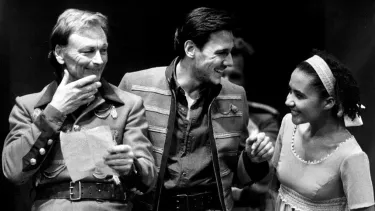 Two men and a woman acting on stage in old fashioned costumes.