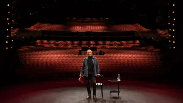 A man standing on stage with an empty audience.