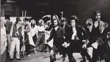 A group of actors on stage wearing old costumes.