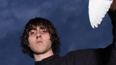 A white man with bowl-cut style hair looks down at the camera holding a white bird.