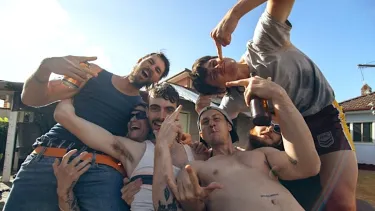 A group of six people posing in front of suburban houses on a sunny day.