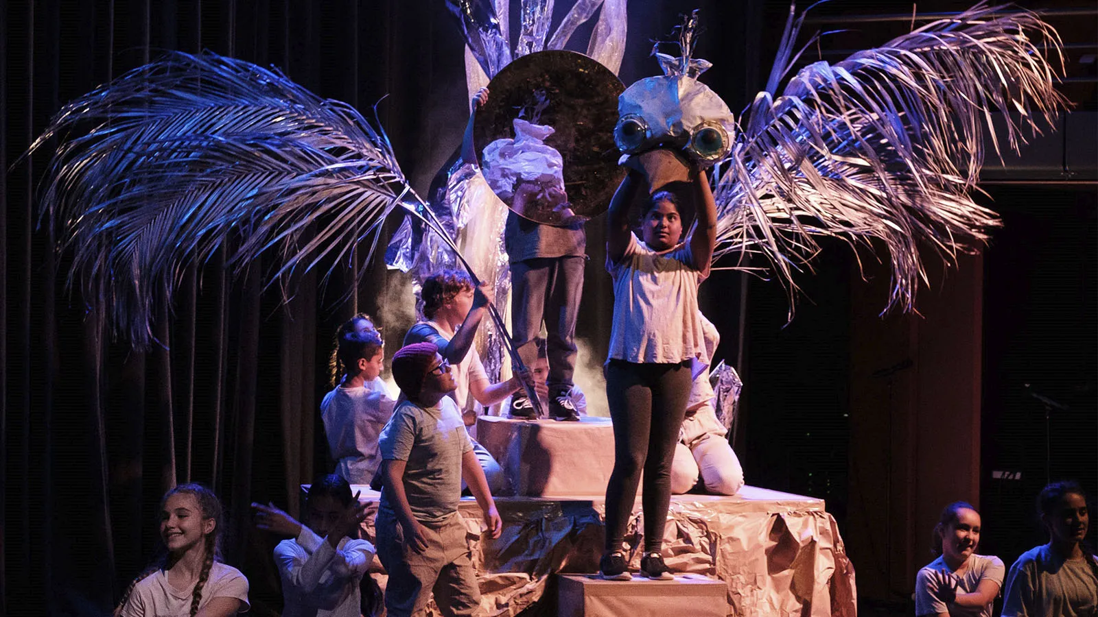 A group of children performing on the stage, holding a big hand made bird.