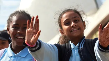 Children in blue school uniforms wave towards the camera.