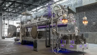 In an industrial envrionment, the steel frame of a bus is decorated with purple and orange lights.