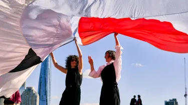 A man and a woman holding a long curtain outside Sydney opera house.