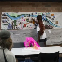 A group of high school students look on to a girl pointing at a poster labelled Nowra.