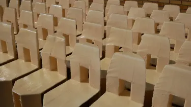 A group of 20 cream chairs with a square cut out in the back sit angled to the left in the sun.