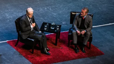 Two middle age men wearing suit, having a debate on the stage.