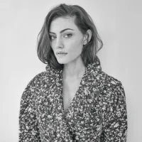Black and white photo of a woman with short, wavy hair wearing a textured coat.