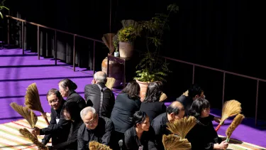 A group of people sitting in a circle with broom sticks in their hands.