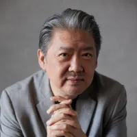 A Chinese man with greying hair in a grey suit looks at the camera.