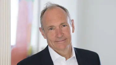 Man in a suit with a kind smile, standing indoors.