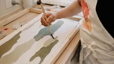 A person in an apron painting a canvas.