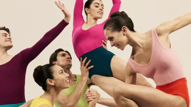 A group of five dancers posed in bright coloured leotards against a light beige background.