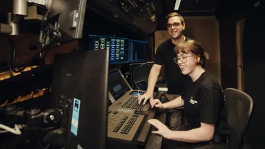 Two trainees in black t shirts look over a soundboard at the Sydney Opera House.