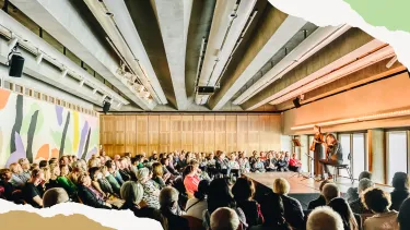 A group of people seated in the Utzon Room watching a performer on stage.